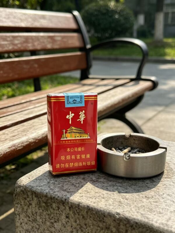Chunghwa Hard Pack Chinese cigarette pack on outdoor stone table next to metal ashtray and park bench premium red tobacco packaging